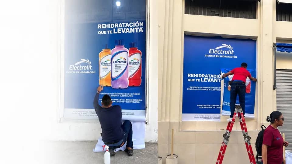Instaladores de Movimark aplicando publicidad de Electrolit en una vitrina